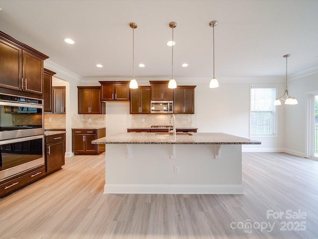 kitchen with appliances with stainless steel finishes, light wood-type flooring, ornamental molding, stone counters, and a breakfast bar