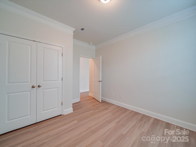 unfurnished bedroom featuring light wood-type flooring, crown molding, baseboards, and a closet