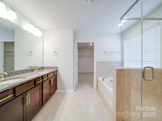 full bath with tile patterned flooring, a bath, double vanity, a walk in closet, and a tile shower
