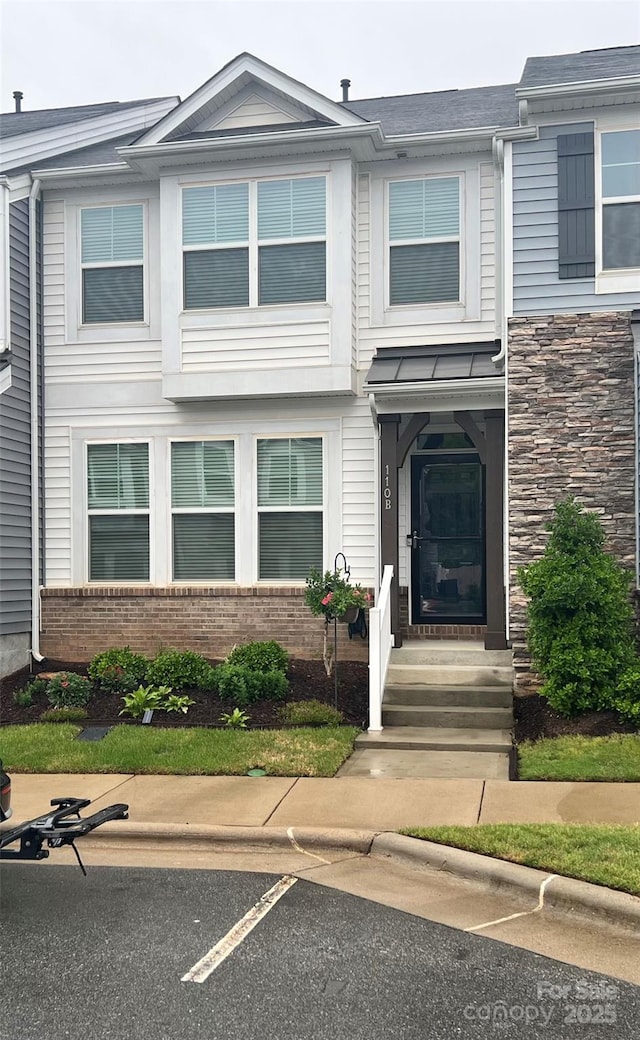 townhome / multi-family property featuring brick siding, stone siding, and uncovered parking