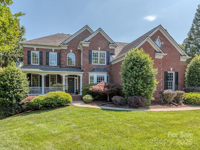 colonial home featuring a front lawn, brick siding, a porch, and roof with shingles