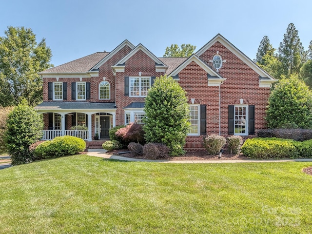 colonial house featuring a front lawn, brick siding, and covered porch