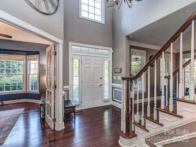 entrance foyer with hardwood / wood-style floors, healthy amount of natural light, stairway, ornamental molding, and a towering ceiling