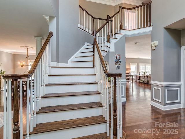 stairway featuring a chandelier, wood finished floors, ornamental molding, and a high ceiling