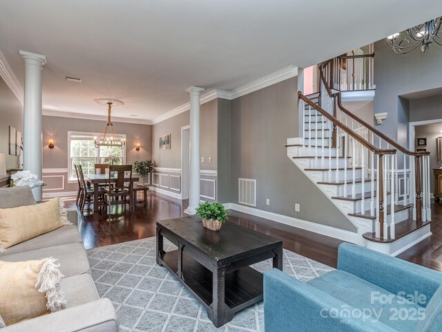 living area with a chandelier, decorative columns, wood finished floors, stairs, and ornamental molding