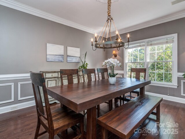 dining room with a chandelier, dark wood finished floors, baseboards, ornamental molding, and wainscoting