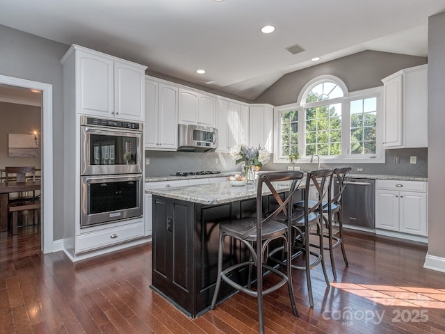 kitchen featuring stainless steel appliances, dark wood-type flooring, white cabinets, light stone counters, and a breakfast bar