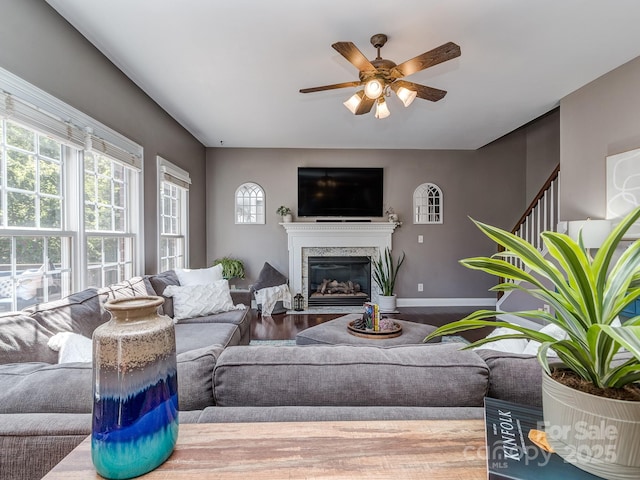 living room featuring a ceiling fan, a fireplace, wood finished floors, baseboards, and stairway