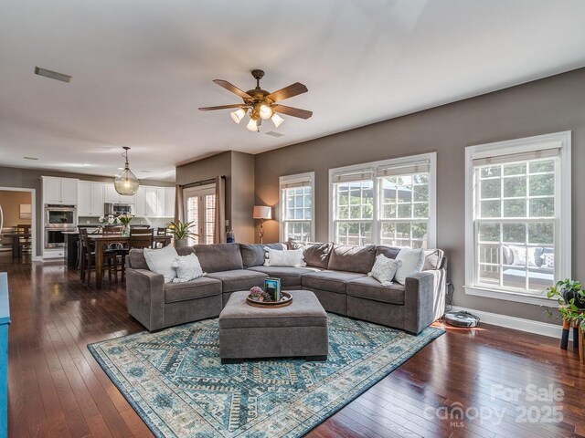 living room with dark wood-type flooring, plenty of natural light, a ceiling fan, and baseboards