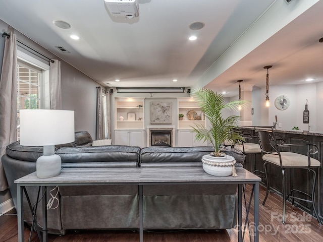 living room featuring wood finished floors, recessed lighting, a fireplace, bar area, and built in shelves