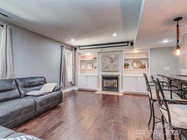 living room with dark wood-style floors, a tile fireplace, recessed lighting, built in features, and baseboards