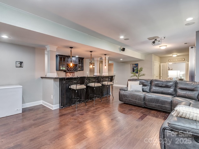 living area with baseboards, bar with sink, dark wood finished floors, and recessed lighting