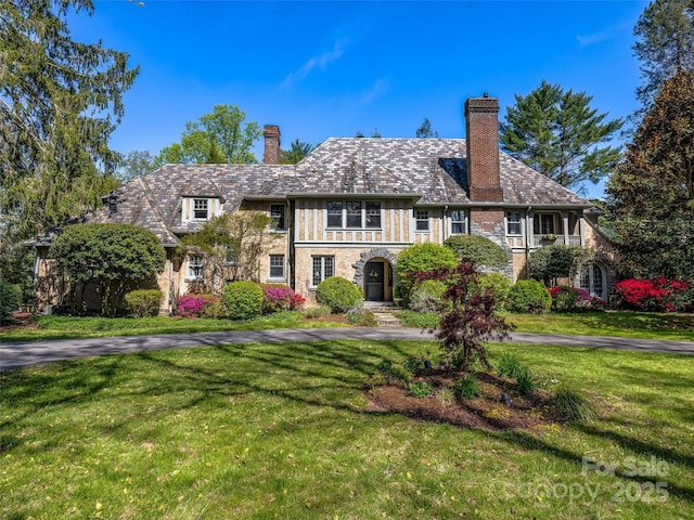 tudor house with a front yard, a chimney, and a high end roof