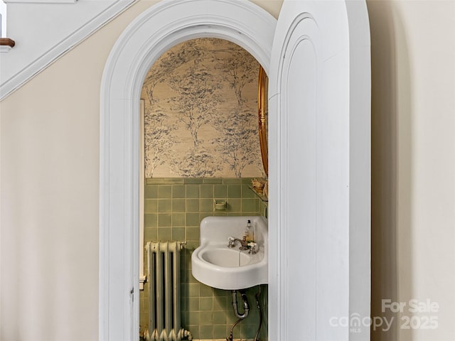 bathroom featuring radiator heating unit, a sink, a wainscoted wall, tile walls, and wallpapered walls
