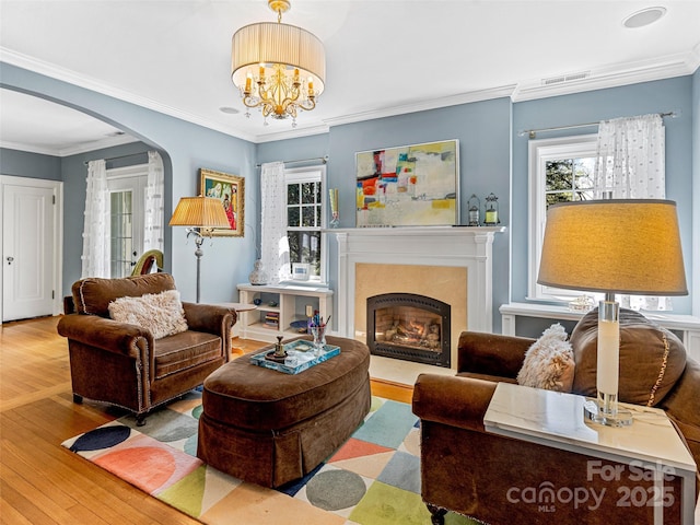 living room featuring arched walkways, wood finished floors, a premium fireplace, crown molding, and a chandelier