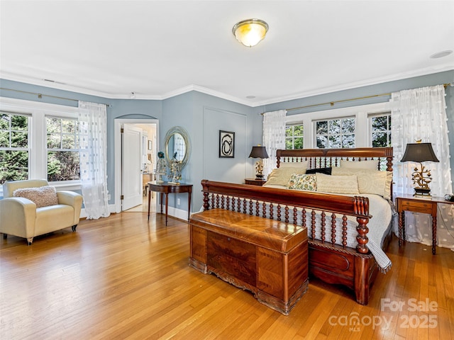 bedroom featuring light wood-style flooring, arched walkways, and crown molding