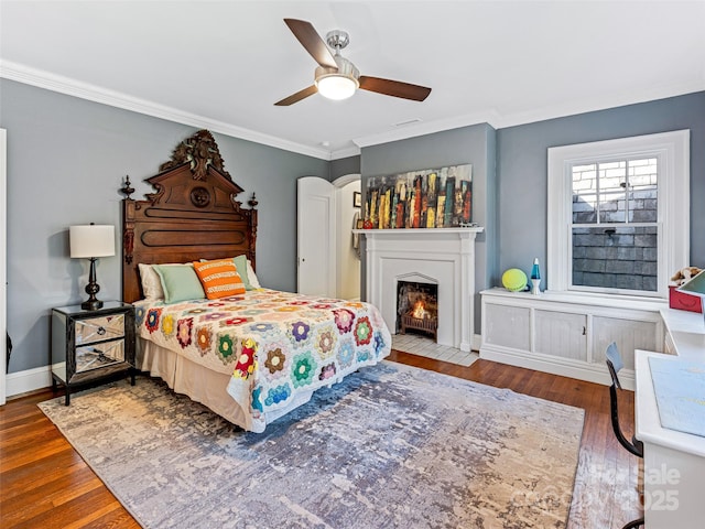 bedroom featuring wood finished floors, ornamental molding, baseboards, a fireplace with flush hearth, and a ceiling fan
