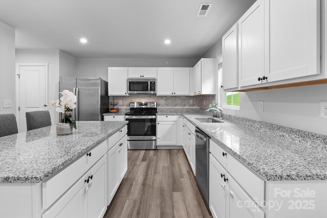 kitchen with stainless steel appliances, a sink, wood finished floors, a kitchen island, and white cabinets