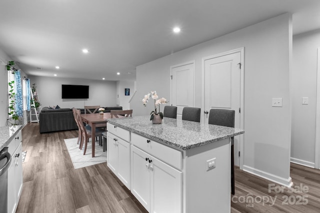 kitchen featuring dark wood-style floors, a center island, white cabinetry, recessed lighting, and light stone counters