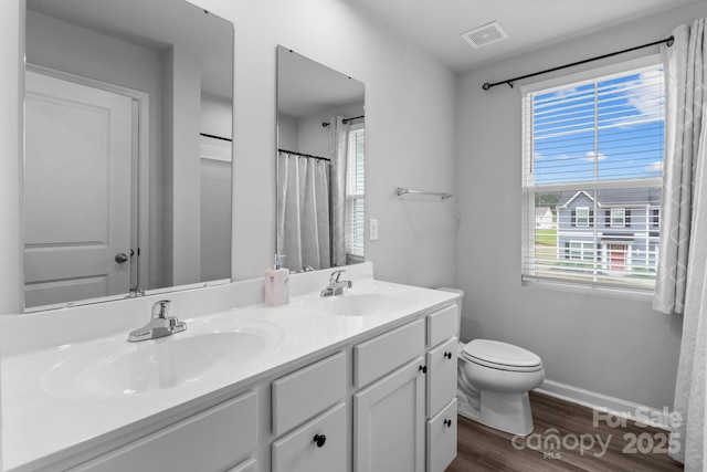 bathroom with wood finished floors, toilet, double vanity, and baseboards