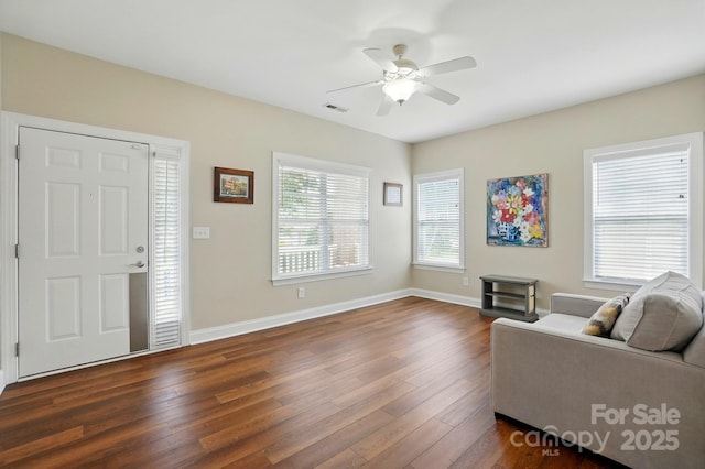 living area with dark wood-type flooring, a ceiling fan, and baseboards