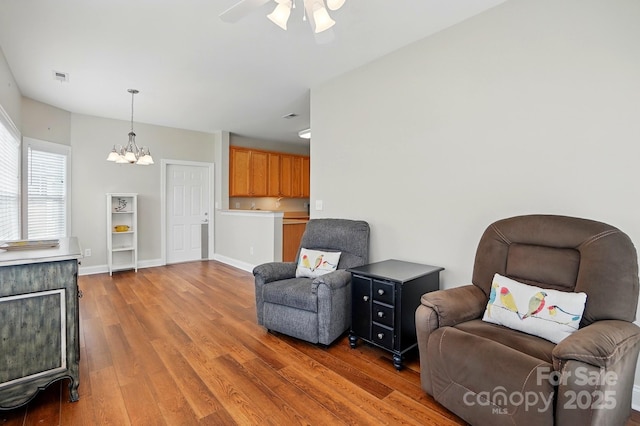 living area featuring light wood-style flooring, a chandelier, a ceiling fan, and baseboards