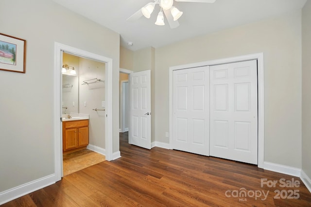 unfurnished bedroom featuring dark wood finished floors, a closet, baseboards, ensuite bathroom, and ceiling fan