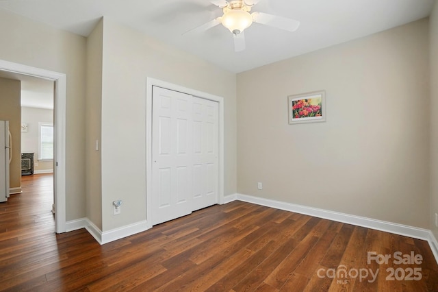unfurnished bedroom with dark wood-style flooring, baseboards, freestanding refrigerator, and a closet