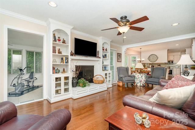 living room featuring ceiling fan, a glass covered fireplace, wood finished floors, healthy amount of natural light, and ornamental molding