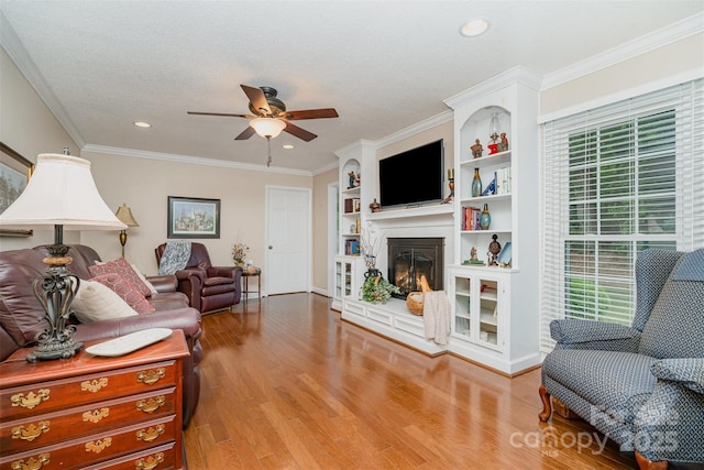 living area featuring a ceiling fan, healthy amount of natural light, wood finished floors, a glass covered fireplace, and recessed lighting