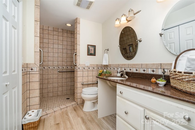 bathroom featuring tile walls, a shower stall, wood finished floors, toilet, and vanity