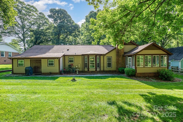 rear view of house featuring a yard, a shingled roof, and a sunroom