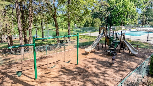 community playground featuring fence, view of scattered trees, and a water view