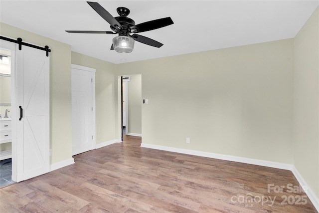 1501 E Church St, Cherryville, NC 28021 - unfurnished bedroom featuring a barn door, wood finished floors, baseboards, and a ceiling fan