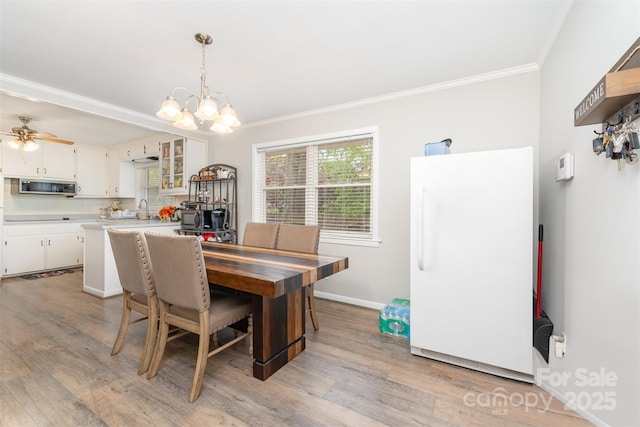 dining area with crown molding, light wood-type flooring, a chandelier, ceiling fan, and baseboards