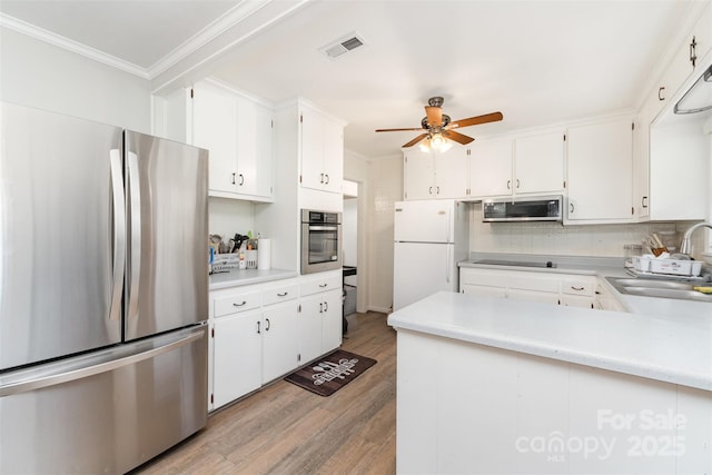 kitchen featuring stainless steel appliances, a sink, ornamental molding, light wood-type flooring, and a ceiling fan