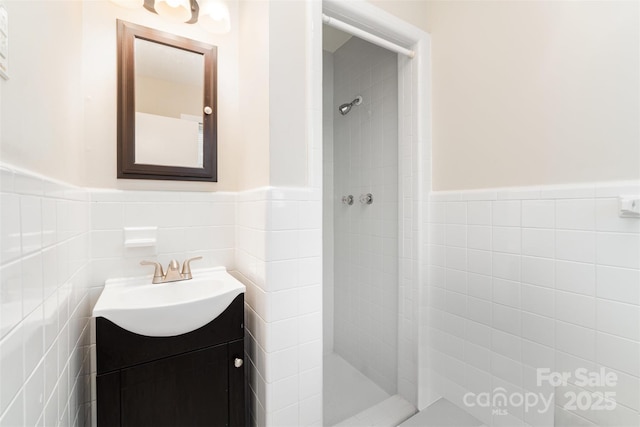 bathroom featuring a tile shower, wainscoting, tile walls, and vanity