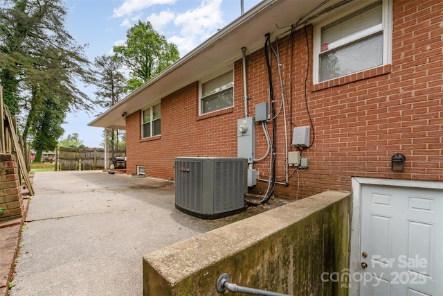 view of home's exterior featuring central AC unit, brick siding, and fence
