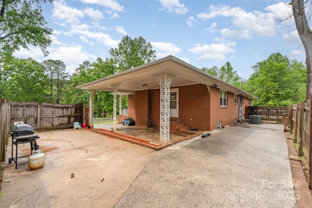view of front facade with brick siding, a patio, central AC, and a fenced backyard