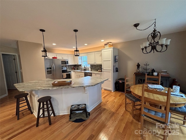 kitchen featuring stainless steel appliances, light wood-style floors, light stone countertops, white cabinetry, and decorative backsplash