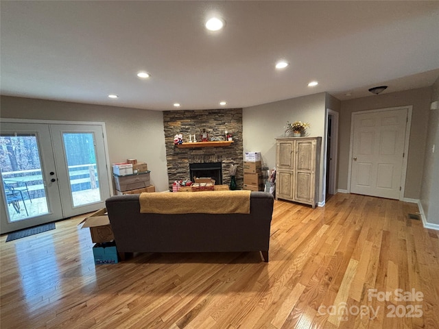 living area featuring light wood-type flooring, recessed lighting, french doors, a stone fireplace, and baseboards