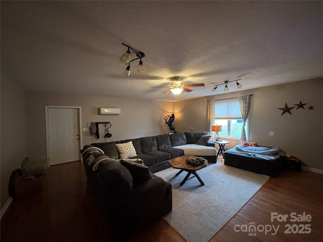 living area featuring rail lighting, a ceiling fan, wood finished floors, a wall unit AC, and a textured ceiling