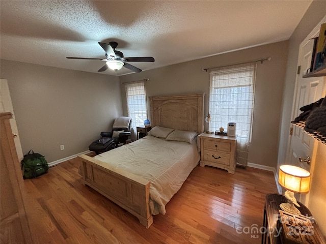 bedroom with light wood-type flooring, baseboards, a textured ceiling, and ceiling fan