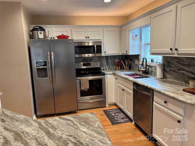 kitchen featuring stainless steel appliances, a sink, light wood finished floors, backsplash, and light stone counters