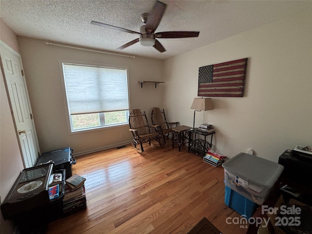 living area with wood finished floors, a ceiling fan, and a textured ceiling