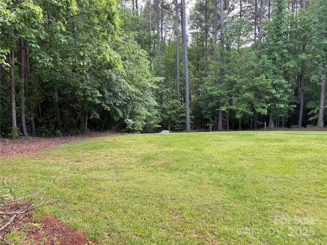 view of green lawn with a forest view