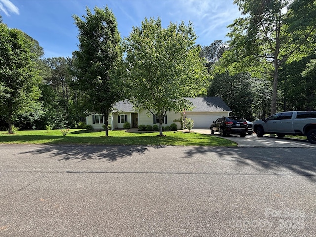 view of property hidden behind natural elements with a front lawn, an attached garage, and driveway