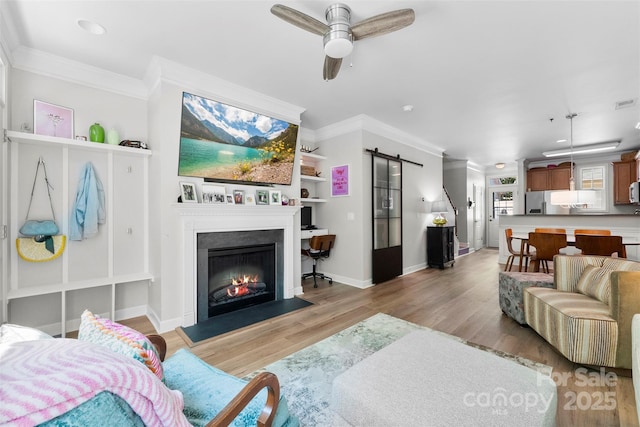 2485 Shanklin Ln, Denver, NC 28037 - living area featuring a barn door, crown molding, light wood-style floors, a glass covered fireplace, and ceiling fan