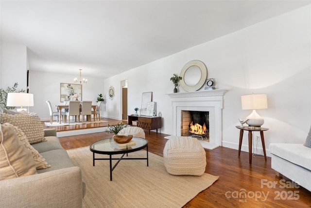living room featuring wood finished floors, a chandelier, a lit fireplace, and baseboards