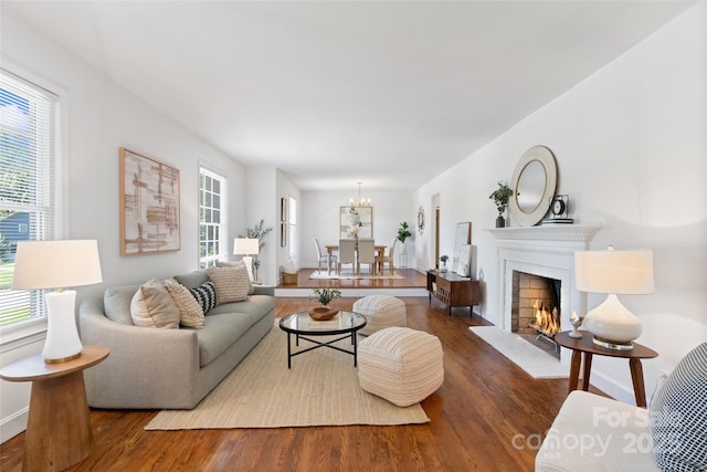 living area with wood finished floors, a warm lit fireplace, a chandelier, and baseboards
